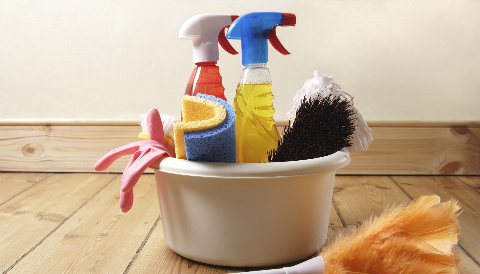 Bowl of cleaning products and feather duster on wooden floor