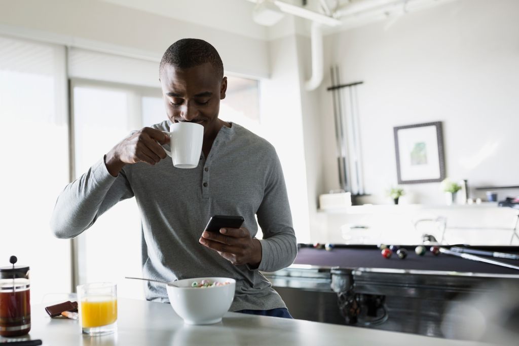 Man sipping morning coffee and texting in kitchen