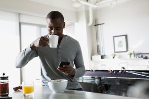 Man sipping morning coffee and texting in kitchen