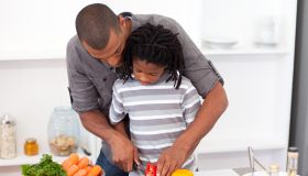 Loving father helping his son cut vegetables in the kitchen