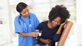 caring young african american nurse offering sick patient water