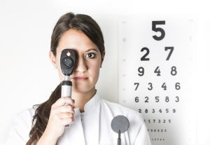 Portrait of young woman looking through ophthalmoscope, close up