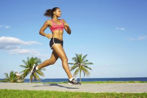 Sporty mixed race woman jogging. Color image, copy space, african american ethnicity female running with green grass and blue sky.