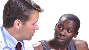 Medical doctor meets with young black male patient with leg brace in clinic with white background