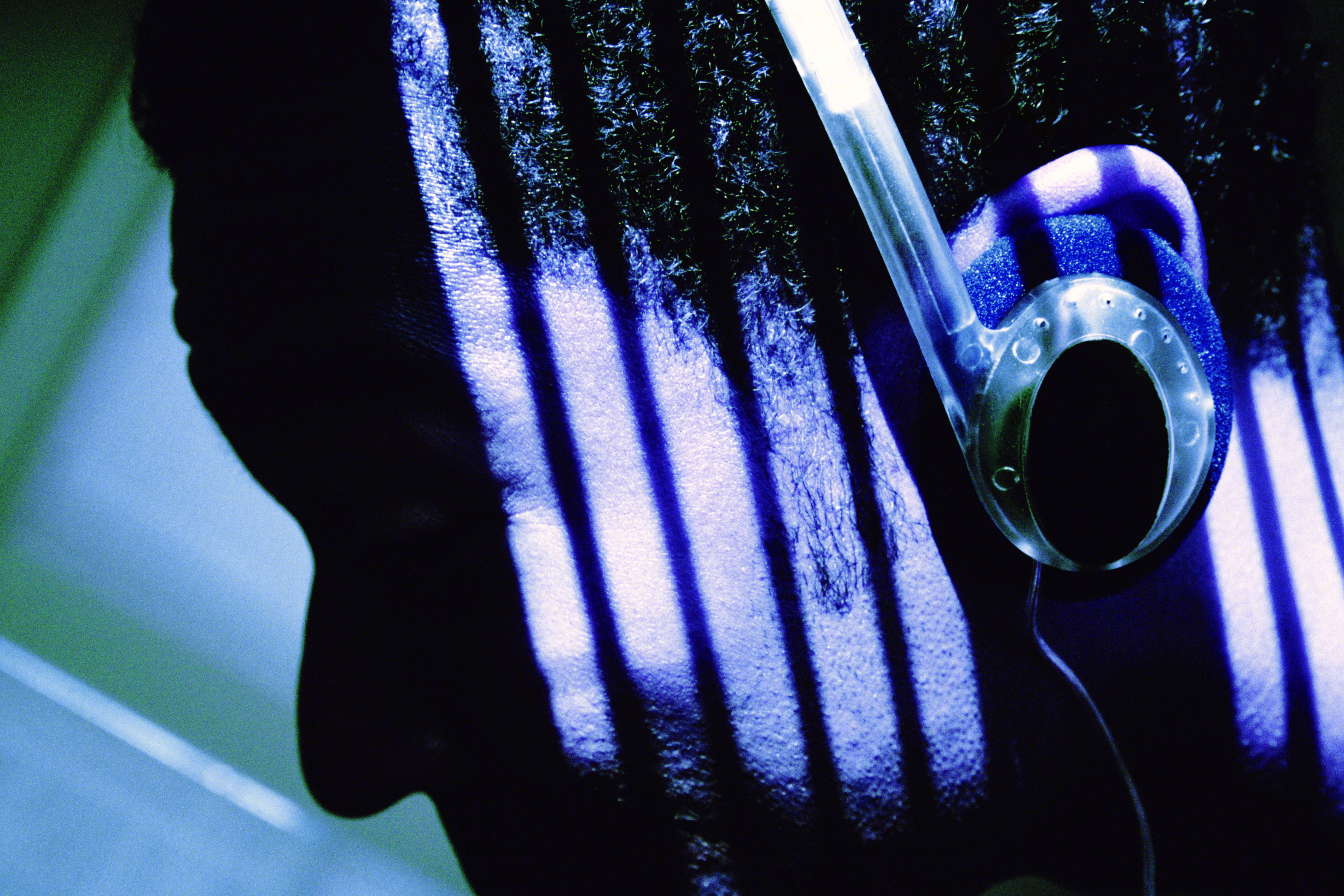 Close-up of man wearing headphones, leaning head on wall near window with blinds