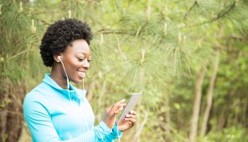 One African descent woman exercising, using cell phone in neighborhood park.
