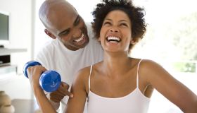 Man smiling at woman lifting weights in living room, woman laughing