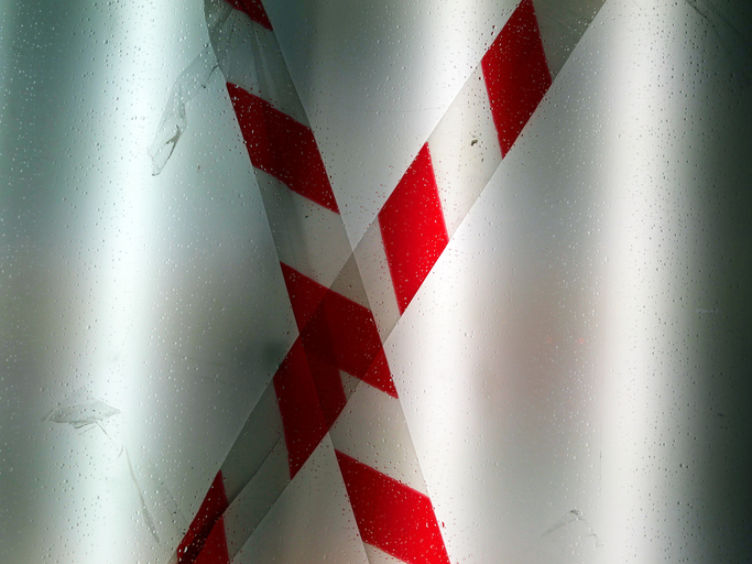 Close-up of a white and red warning tape crossed on an illuminated, white and opaque window in Brussels, Belgium. Electric light. Natural colors and shadow.
