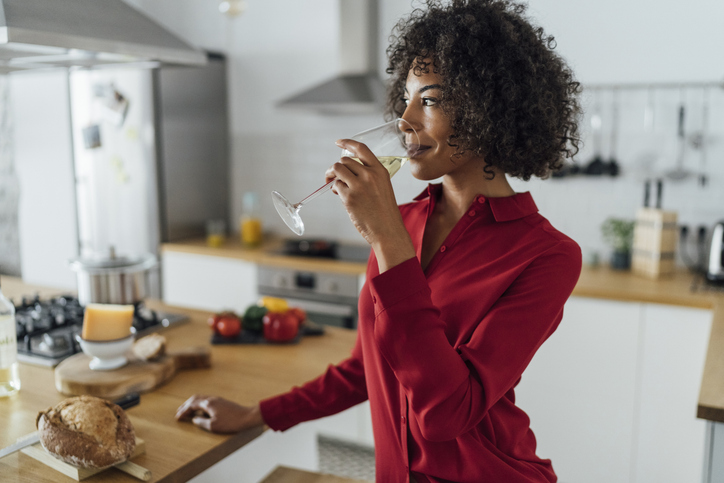 Woman standing in kitchen, drinking a glass of white wine