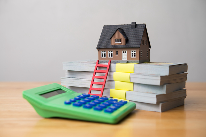 House model, red ladder, stack banknotes and calculator on wooden table white wall background.