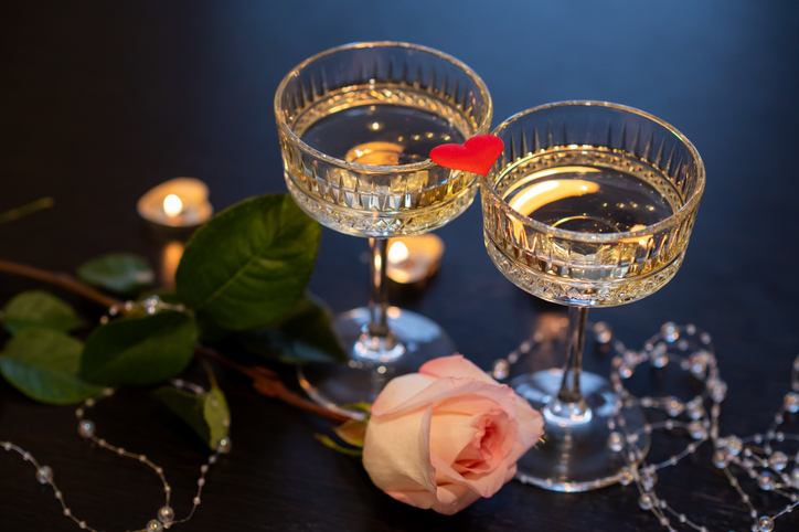 Romantic Valentine's Day still life with champagne glasses, pink rose, candles and red heart on dark background