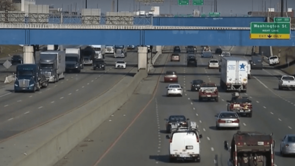 Busy highway with multiple lanes of traffic, including cars, trucks, and a police vehicle. "Washington St." sign visible.