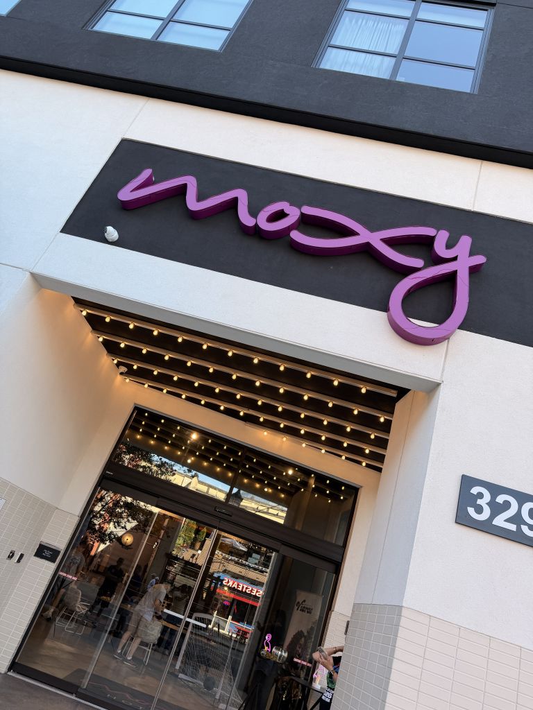 Large purple "Macy's" sign above a storefront with string lights and a view of the street outside.