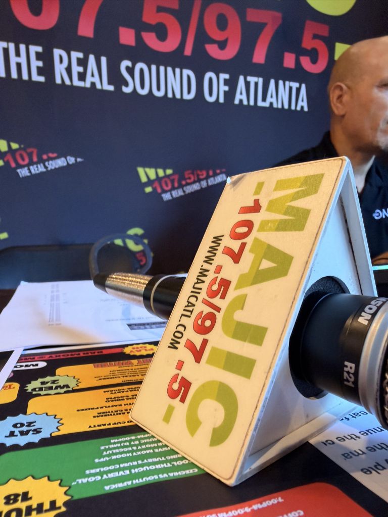 Radio station branding and equipment, including a microphone and a sign for "107.5 The Real Sound of Atlanta".