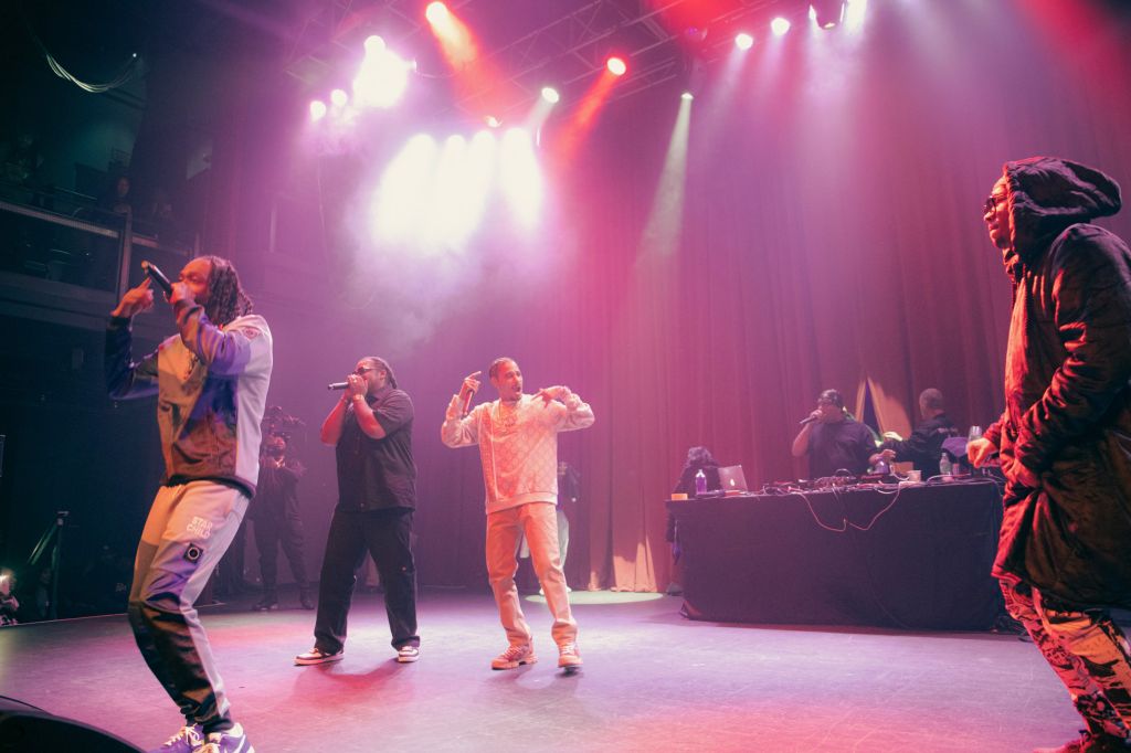 A group of musicians performing on a brightly lit stage, with colorful lighting and smoke effects creating an energetic atmosphere.
