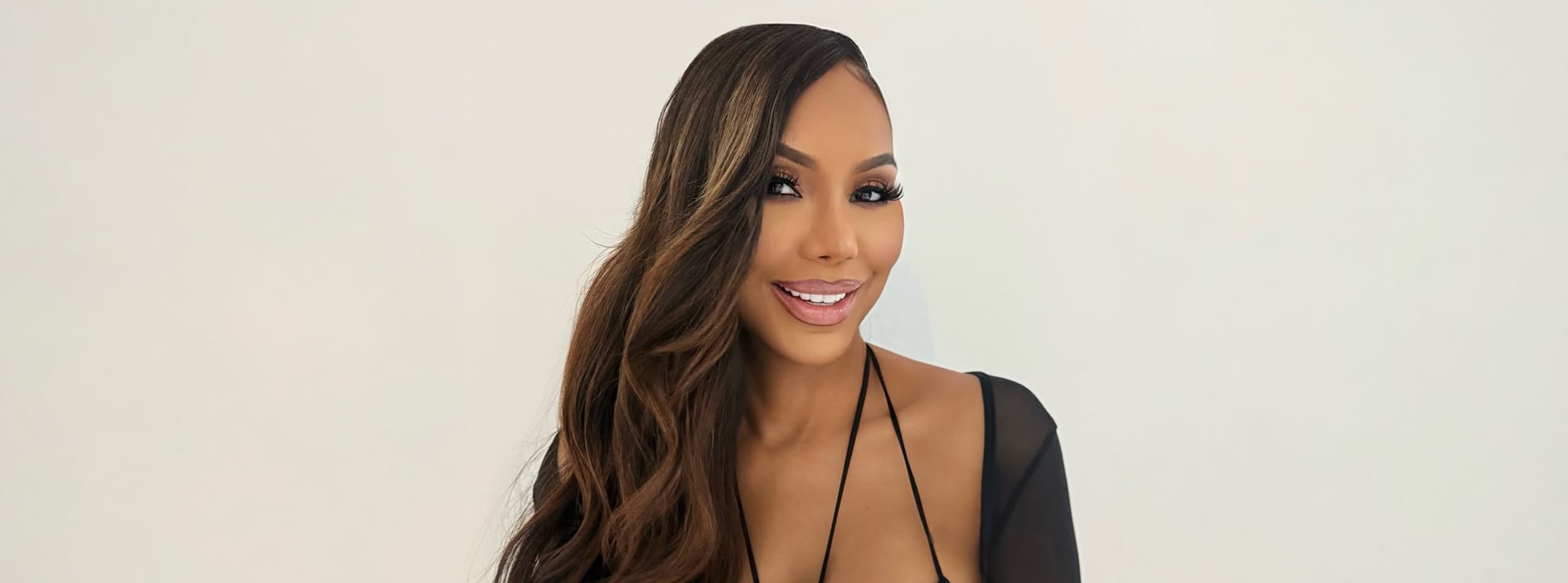 A smiling woman with long, wavy brown hair wearing a black swimsuit top.
