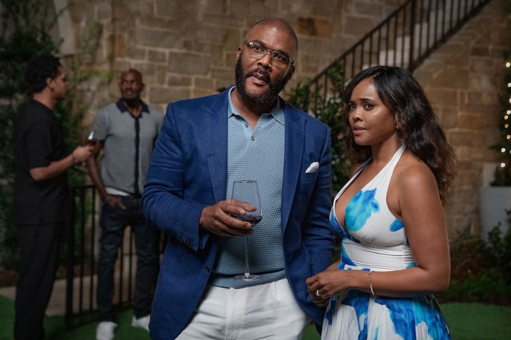 Two people, a man and a woman, standing together outdoors at night. The man is wearing a blue suit and the woman is wearing a blue and white patterned dress.