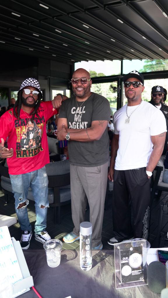 Four men standing together, one wearing a red shirt with a graphic design, another wearing a black shirt that says "Call my agent", and two others wearing casual clothing. They appear to be in a casual setting.