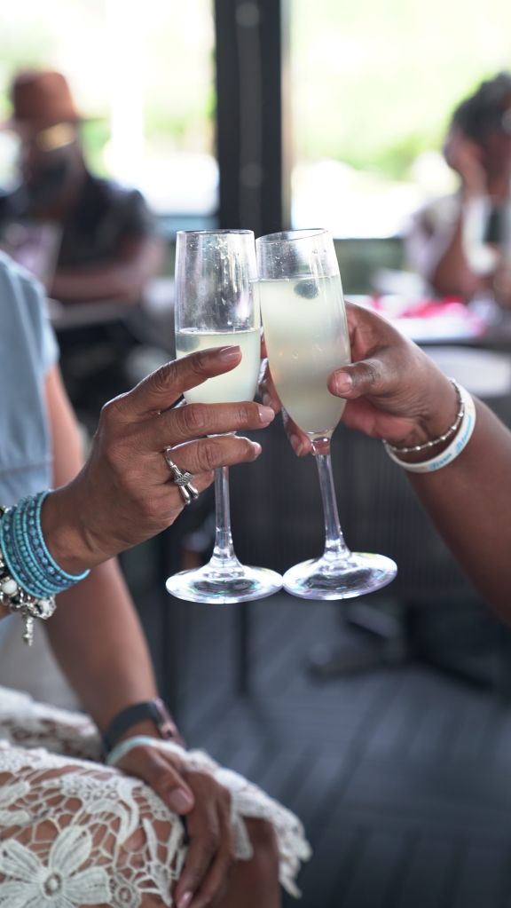 Two hands holding champagne flutes, celebrating with drinks in a blurred indoor setting.