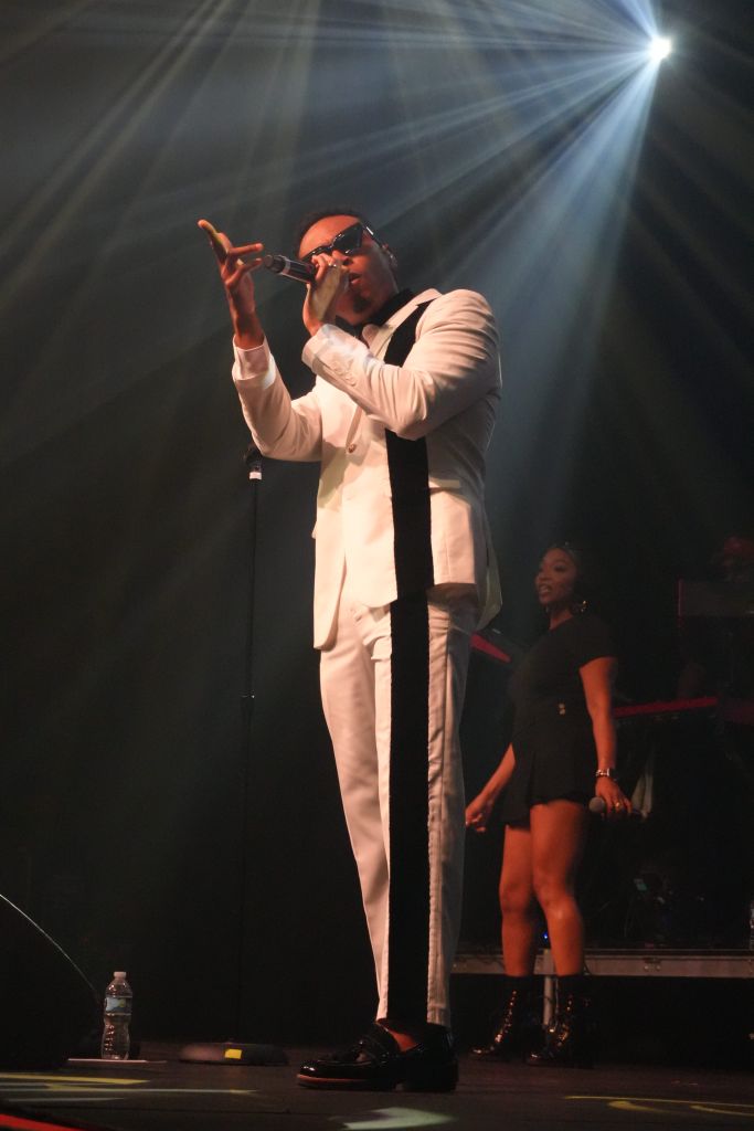 A performer in a white suit singing into a microphone on stage, with spotlights shining on them.